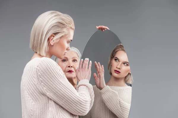 Short-haired blonde curious girl in knitted sweater touching surface of mirror — Stock Photo, Image