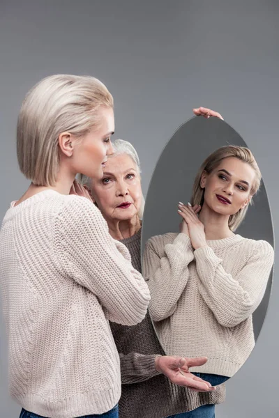 Blonde jonge dame glimlachen terwijl het zoeken in ronde spiegel — Stockfoto