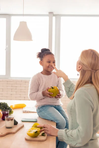 Leuk vrolijk meisje peper terwijl helpen moeder koken houden — Stockfoto