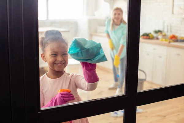 Piccola ragazza carina sorridente mentre aiuta sua madre con la pulizia — Foto Stock