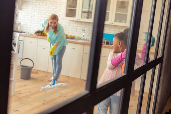 Mother mopping the floor and looking at her helpful daughter — Stock Photo, Image