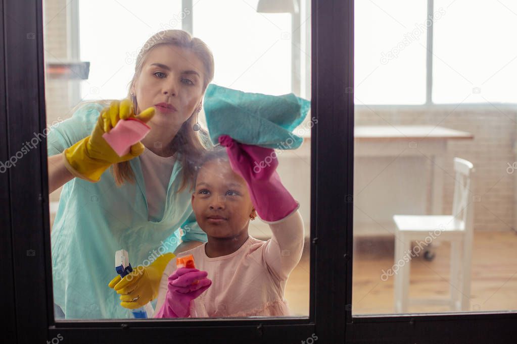 Mother and daughter feeling busy while cleaning the glass door