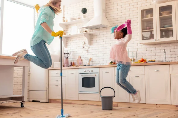 Mãe e filha pulando enquanto limpam o chão — Fotografia de Stock