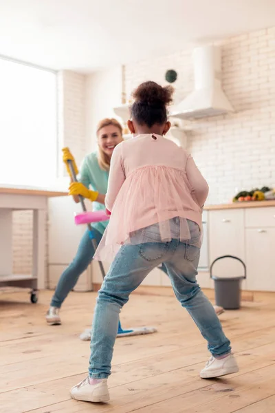 Graziosa figlia riccia che pulisce il pavimento con madre e danza — Foto Stock