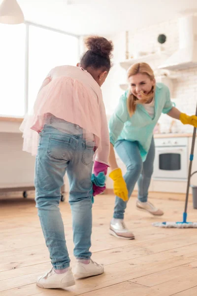 Mother and daughter dancing and moving while cleaning the kitchen — Stock Photo, Image