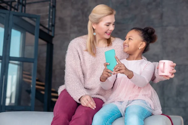 Блимає приваблива дівчина тримає синій смартфон, сидячи поруч з мамою — стокове фото