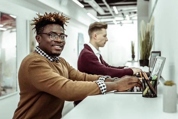 Rozpromieniony African American facet w jasne okulary praca na laptopie — Zdjęcie stockowe