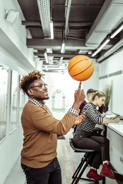 Sorrindo positivo afro-americano cara jogando com bola de basquete no escritório — Fotografia de Stock