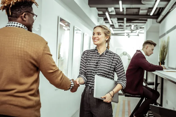 Fröhliche junge Dame im schwarz-weißen Hemd begrüßt neue Arbeitskollegin — Stockfoto