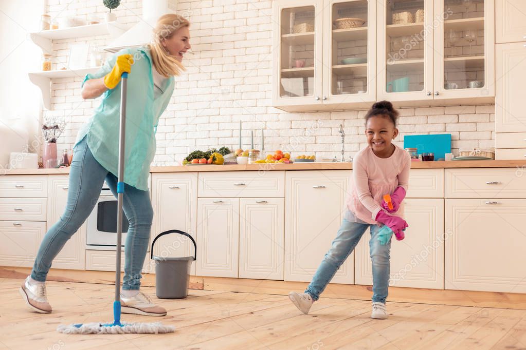 Cheerful foster daughter laughing while cleaning kitchen with mom