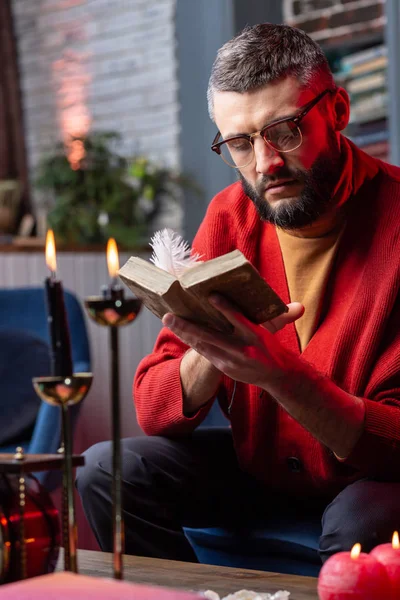 Μέντιουμ, ανάγνωση βιβλίο αστρολογία που κάθεται στο τραπέζι με κεριά — Φωτογραφία Αρχείου
