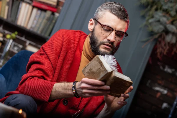 Barbudo adivino maduro usando pulsera sosteniendo poco viejo libro de mago — Foto de Stock