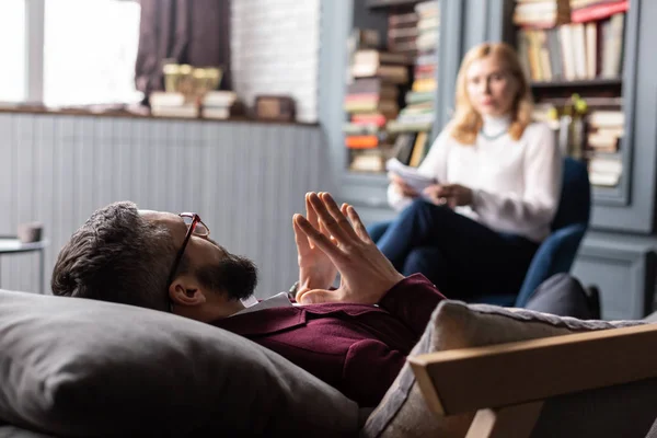 Bearded man in glasses lying on sofa while talking to therapist — Stock Photo, Image