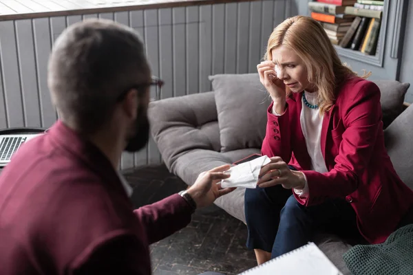 Terapeuta útil que da servilleta al cliente sintiéndose emocional y llorando — Foto de Stock