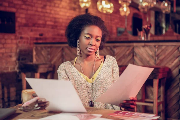 Aantrekkelijke Afro-Amerikaanse ontwerper controleren schetsen terwijl het besteden van tijd in de coffeeshop. — Stockfoto