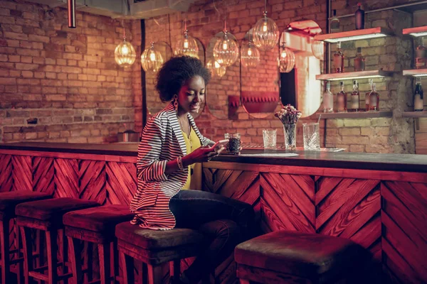 Ravishing gorgeous African-American female checking phone while holding drink