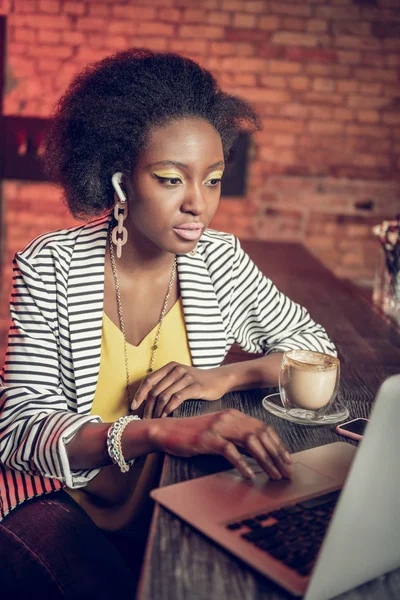 Allvarlig Afro-American tjugo år gammal flicka arbetar på laptop på bardisk — Stockfoto