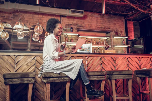 Bewitching barmaid thoroughly reading menu while sitting at bar chair