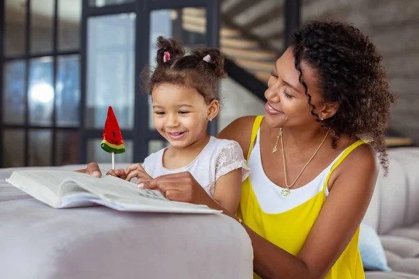 Encantadora niña internacional leyendo libro con su mamá — Foto de Stock