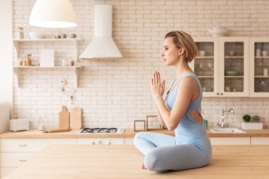 Lotus duruş mutfak masasında oturan sakin ve huzurlu kısa saçlı kadın