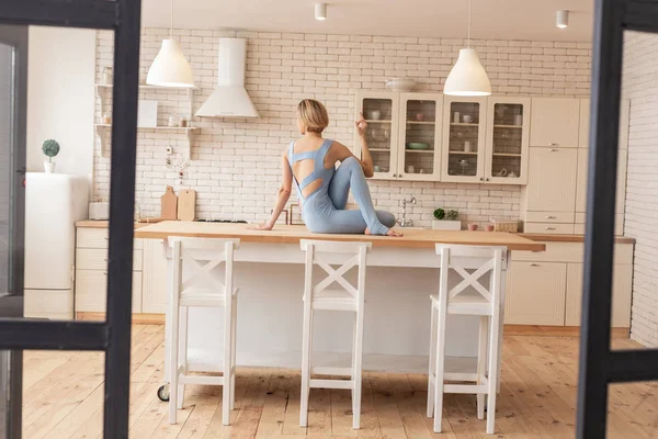 Flexible resolute young girl composing unusual poses on kitchen working surface