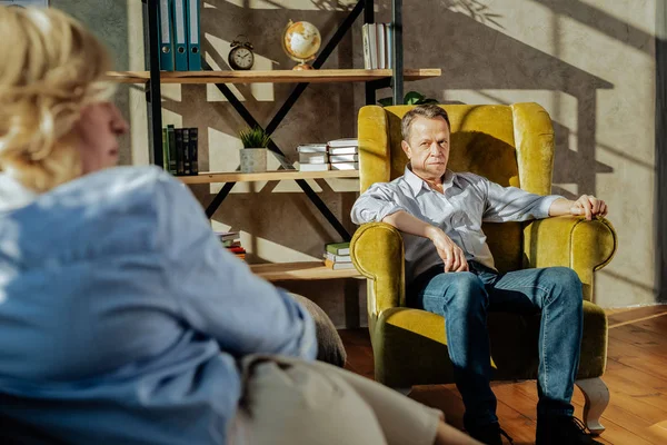 Resolute short-haired man in blue jeans sitting in front of his wife — Fotografie, imagine de stoc