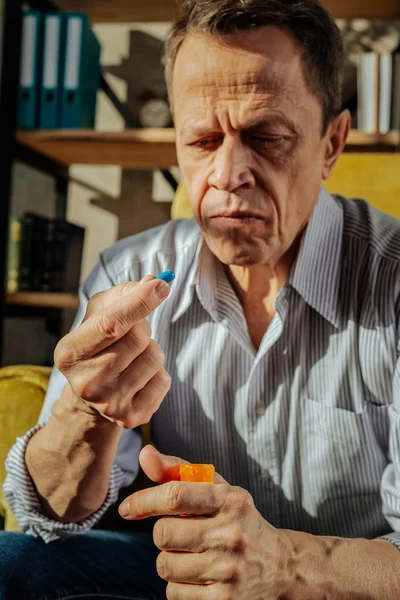 Enfocado viejo hombre molesto sosteniendo un recipiente naranja con pastillas — Foto de Stock