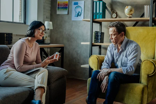 Smiling good-looking therapist proposing container with pills