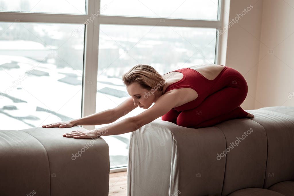 Peaceful blonde appealing gymnast compactly folding on couch back