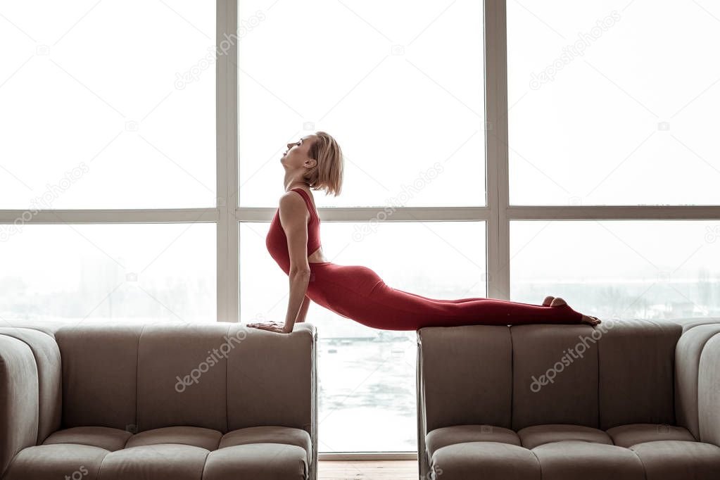 Appealing strong woman in bright red outfit performing yoga