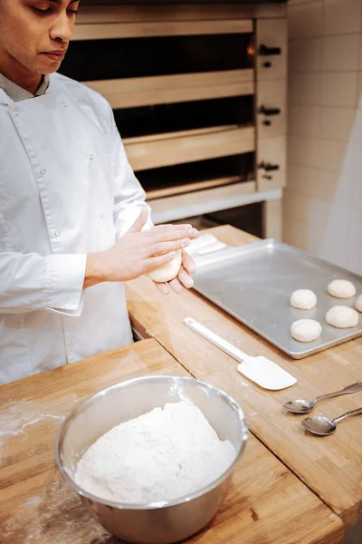 Baker adicionando um pouco de farinha enquanto forma pequenos pães redondos — Fotografia de Stock