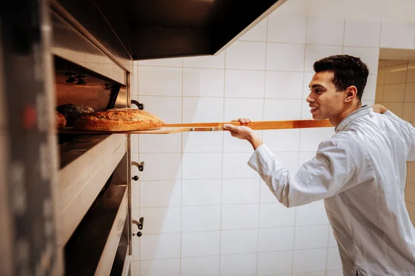 Baker sorrindo enquanto toma baguetes fora do forno — Fotografia de Stock