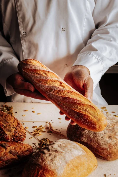 Baker standing near table and showing little wheat baguette