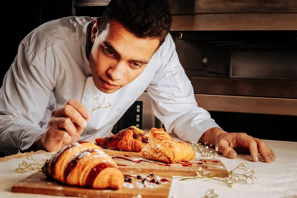 Baker inclinado na mesa e olhando para sobremesas incríveis — Fotografia de Stock