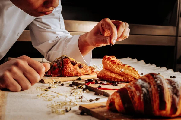 Bäcker verziert Croissants und Windbeutel auf Holztellern — Stockfoto