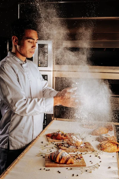 Baker renversant du sucre en poudre sur des croissants et des bouffées — Photo