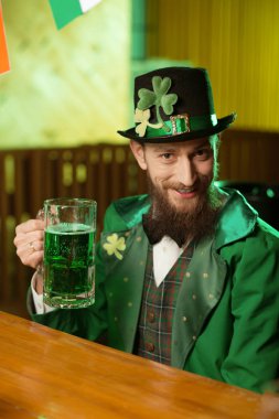 Koyu renk saçlı sakallı genç adam bir bardak yeşil bira ile elinde tutan bir yeşil kostüm