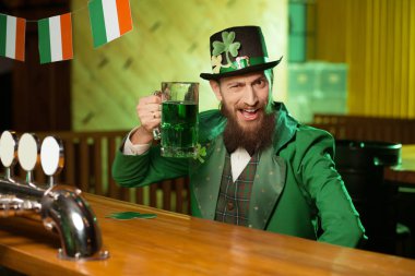 Esmer genç adam cüce şapkası ile İrlandalı barda oturan shamrock sakallı
