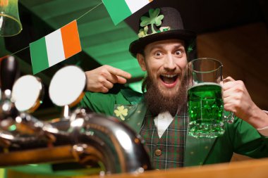 Koyu renk saçlı sakallı genç adam bir bardak yeşil bira gösterilen bir masal cini kostümü