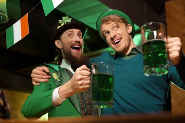 Koyu renk saçlı sakallı genç adam cüce şapkası ve arkadaşı yeşil bira içmek