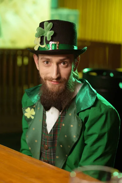 Giovane barbuto dai capelli scuri in costume verde seduto a tavola in un caffè — Foto Stock