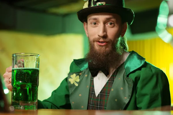 Jeune homme barbu aux cheveux foncés en costume vert avec un symbole de trèfle assis à la table — Photo