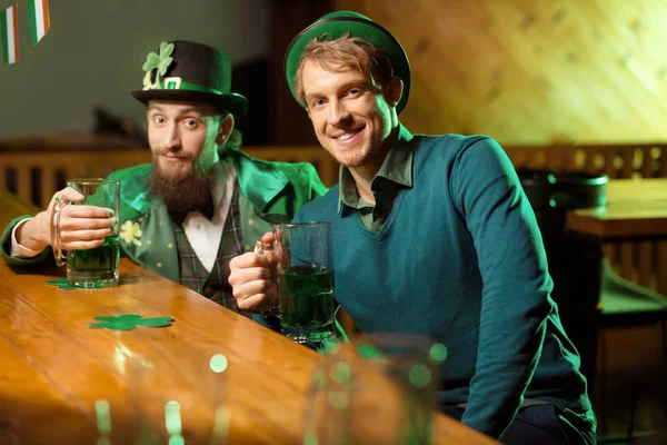 Giovane bel ragazzo dai capelli biondi con un cappello verde che tiene in mano un bicchiere di birra verde — Foto Stock