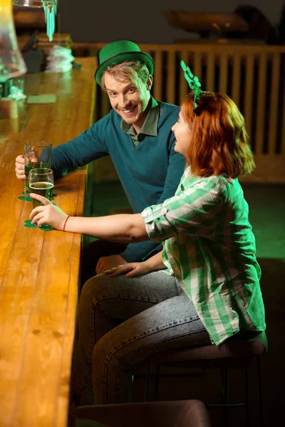 Joven guapo de pelo rubio con un sombrero verde y una chica pelirroja sentada en el mostrador del bar — Foto de Stock
