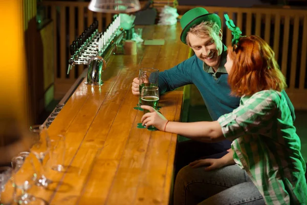 Fair-haired young handsome man in a green hat and a red-haired girl talking at the bar