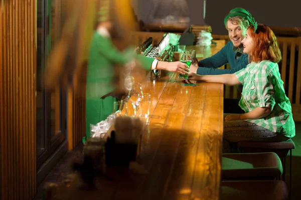 Bruno barbuto giovane uomo in un cappello leprecauno dando un bicchiere di birra a una ragazza — Foto Stock