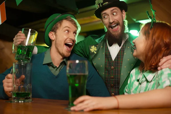 Chica guapa pelirroja con una camisa verde a cuadros y hombres con disfraces de día de San Patricio riéndose juntos — Foto de Stock