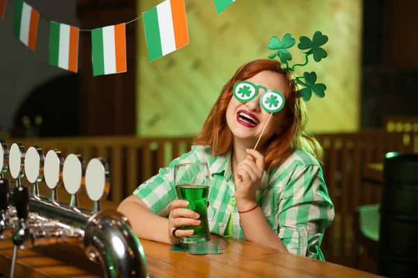 Red-haired pretty girl in a green checkered shirt having fun with eyewear with shamrock symbols — Stock Photo, Image
