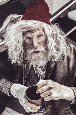 Yaşlı serseri bir şey süre oturan ve kamera üzerinden bakarak konuşuyor.