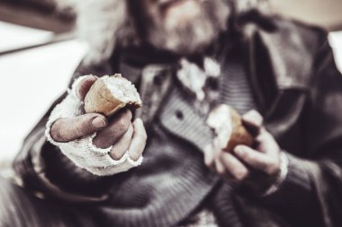 Close up photo of the homeless man holding two pieces of baking with both hands. clipart